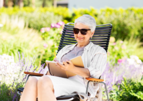 Elderly Lady sitting in the garden reading in the sun
