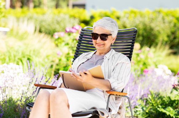 Elderly Lady sitting in the garden reading in the sun