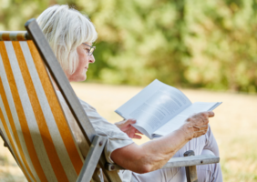 Elderly woman sitting in beach chair reading a book