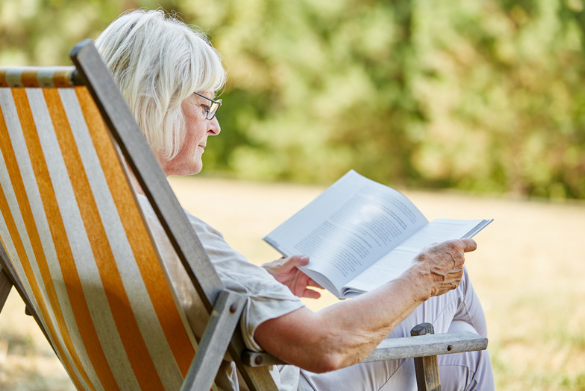 Elderly woman sitting in beach chair reading a book